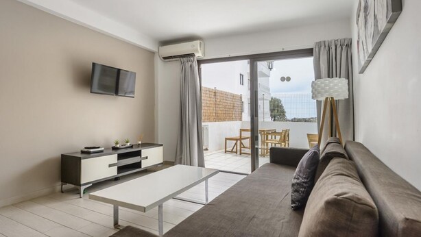 Een moderne woonkamer met een bank, een televisie, een eettafel en een balkon met tuinmeubilair.
