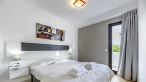 Een moderne hotelkamer met een groot bed, nachtkastjes met lampen, een schilderij aan de muur en uitzicht door een deur.