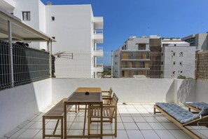 Une terrasse sur le toit, avec une table et des chaises, un coin salon confortable et une vue sur les bâtiments environnants.