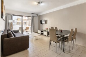 Un salon moderne comprenant un canapé, une table à manger, des chaises, un téléviseur à écran plat et un balcon offrant une vue sur les immeubles.