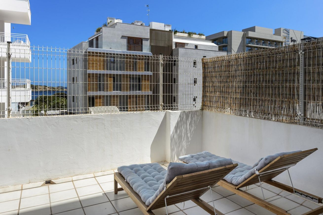 Una terraza en la azotea con dos sillones de descanso, una pared blanca y vistas a edificios al fondo.