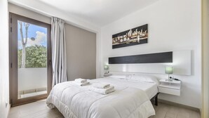 A hotel room with a large bed, a view through a sliding door, a painting on the wall, and a nightstand with a lamp.