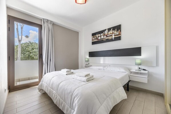 Une chambre d’hôtel avec un grand lit, une vue par une porte coulissante, un tableau au mur et une table de chevet avec une lampe.