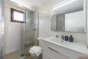 Une salle de bain moderne avec une douche à parois de verre, des toilettes blanches, un lavabo avec un miroir au-dessus et un porte-serviettes.