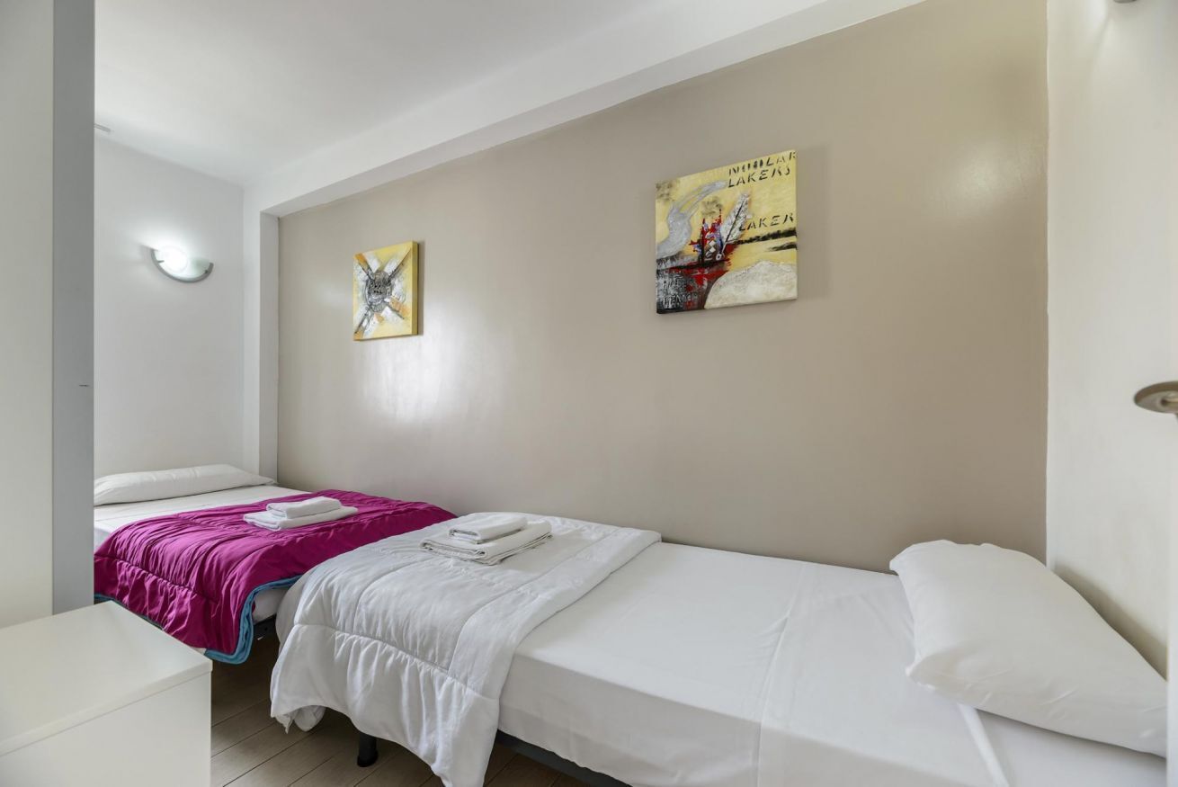 Una habitación con dos camas, una pared blanca y dos obras de arte.