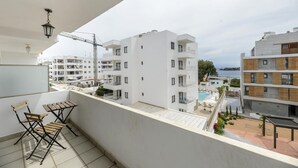 A balcony with a view of a modern building complex, a pool, and a crane in the background. - Esmeralda apartment in Ibiza!!! 201 (Ibiza / Eivissa)