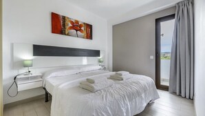 A modern hotel room with a large bed, a bedside table with a lamp, a painting on the wall, and a view through a door. - Esmeralda apartment in Ibiza!!! 201 (Ibiza / Eivissa)