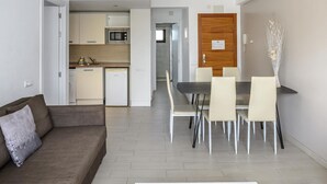 A modern living room with a sofa, a dining table with chairs, a kitchen area with appliances, and a wooden door. - Esmeralda apartment in Ibiza!!! 201 (Ibiza / Eivissa)