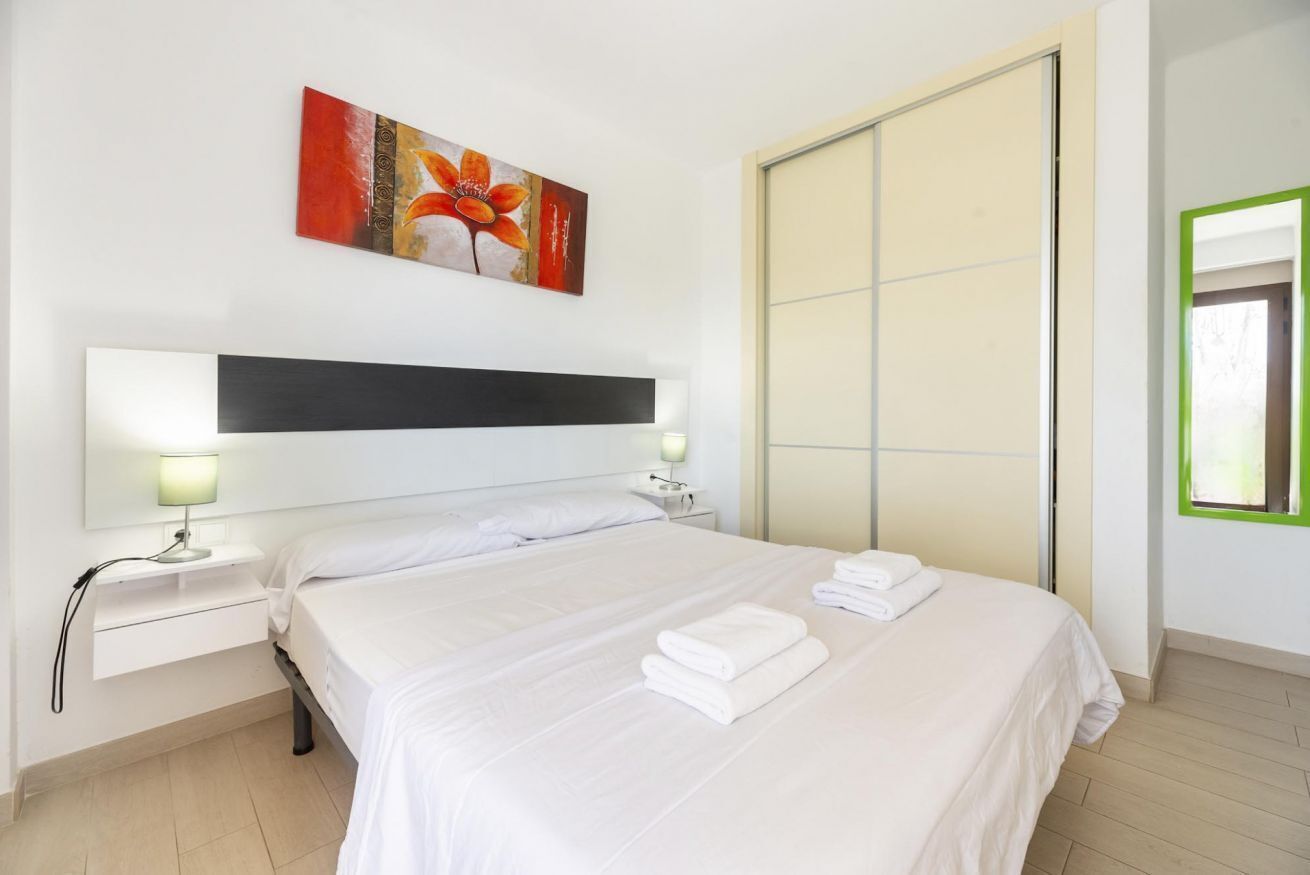 Habitación de hotel con una cama grande, dos mesitas de noche con lámparas, una obra de arte colgada en la pared, una puerta corredera y un ventanal con marco verde.
