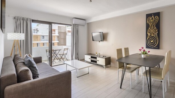 A modern living room with a sofa, coffee table, TV, dining table, and chairs. - Esmeralda apartment in Ibiza!!! 202 (Ibiza / Eivissa)