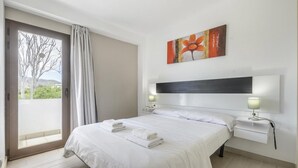 A hotel room with a large bed, a nightstand, a lamp, a painting, and a view through a glass door. - Esmeralda apartment in Ibiza!!! 202 (Ibiza / Eivissa)