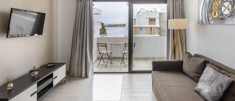 Ein modernes Wohnzimmer mit Flachbildfernseher, einer Couch, einem Couchtisch und einem Balkon mit Meerblick.