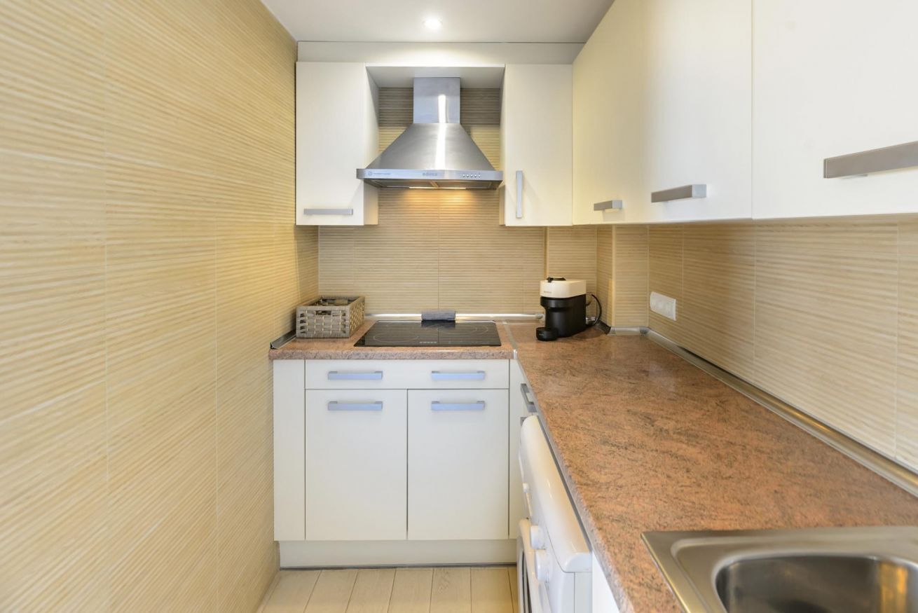 A compact kitchen with white cabinets, a stainless steel range hood, a coffee maker, and a built-in oven.