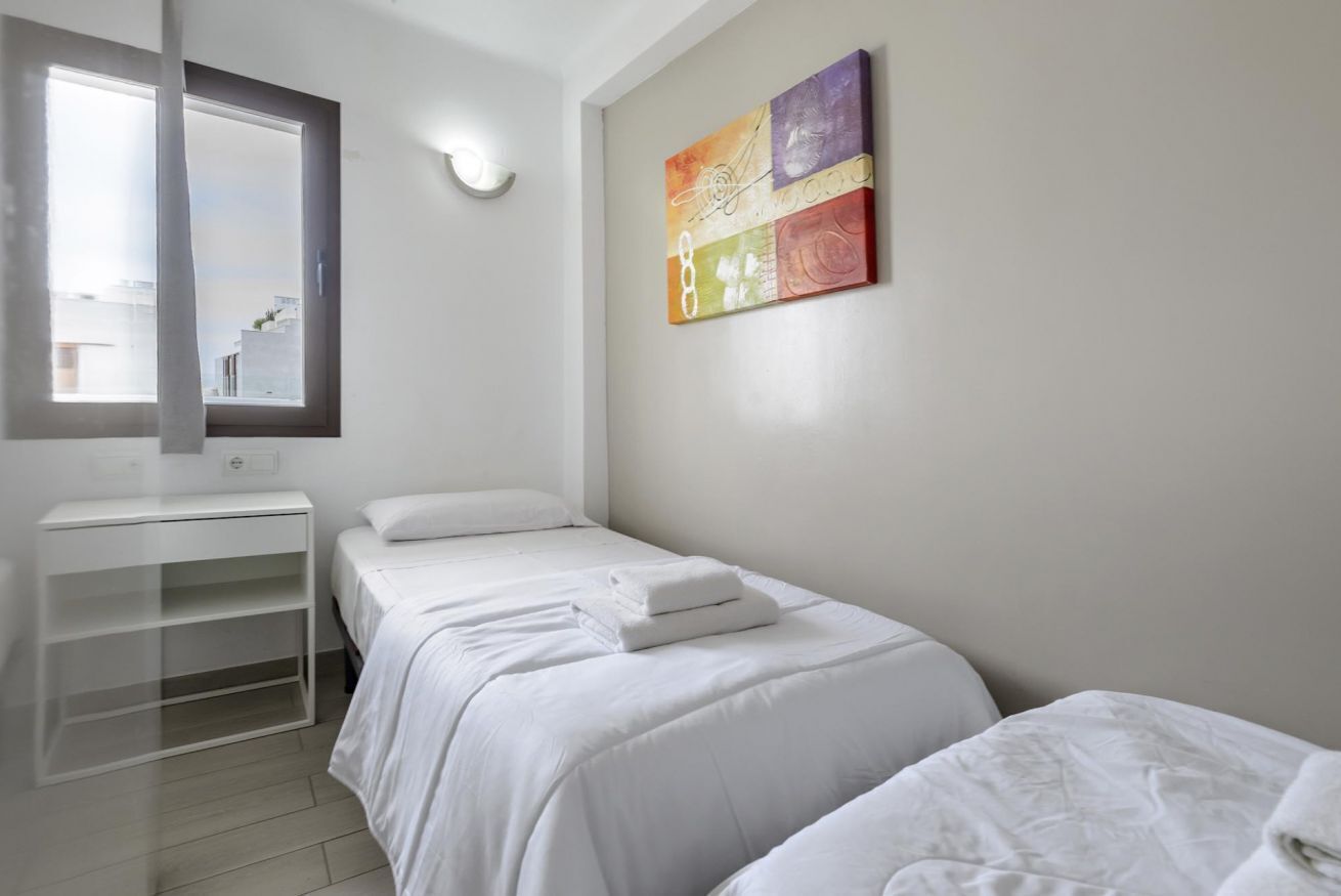 A bedroom with two beds, a window, a bedside table, and a wall-mounted artwork.