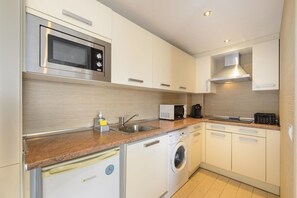 A compact kitchen with a built-in microwave, a coffee maker, a washing machine, and a dishwasher.