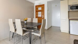 Un coin repas avec une table et des chaises, une porte en bois recouverte de papiers et une cuisine équipée d’appareils électroménagers.