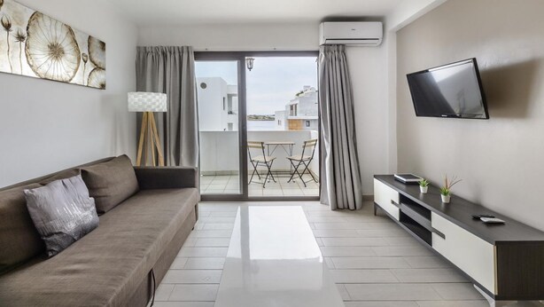 Un salon moderne avec un canapé, un téléviseur et une vue sur un balcon extérieur.