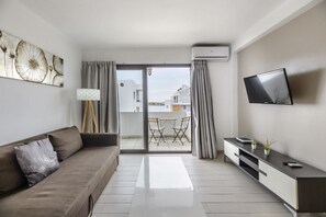A modern living room with a sofa, TV, and a view to an outdoor balcony.