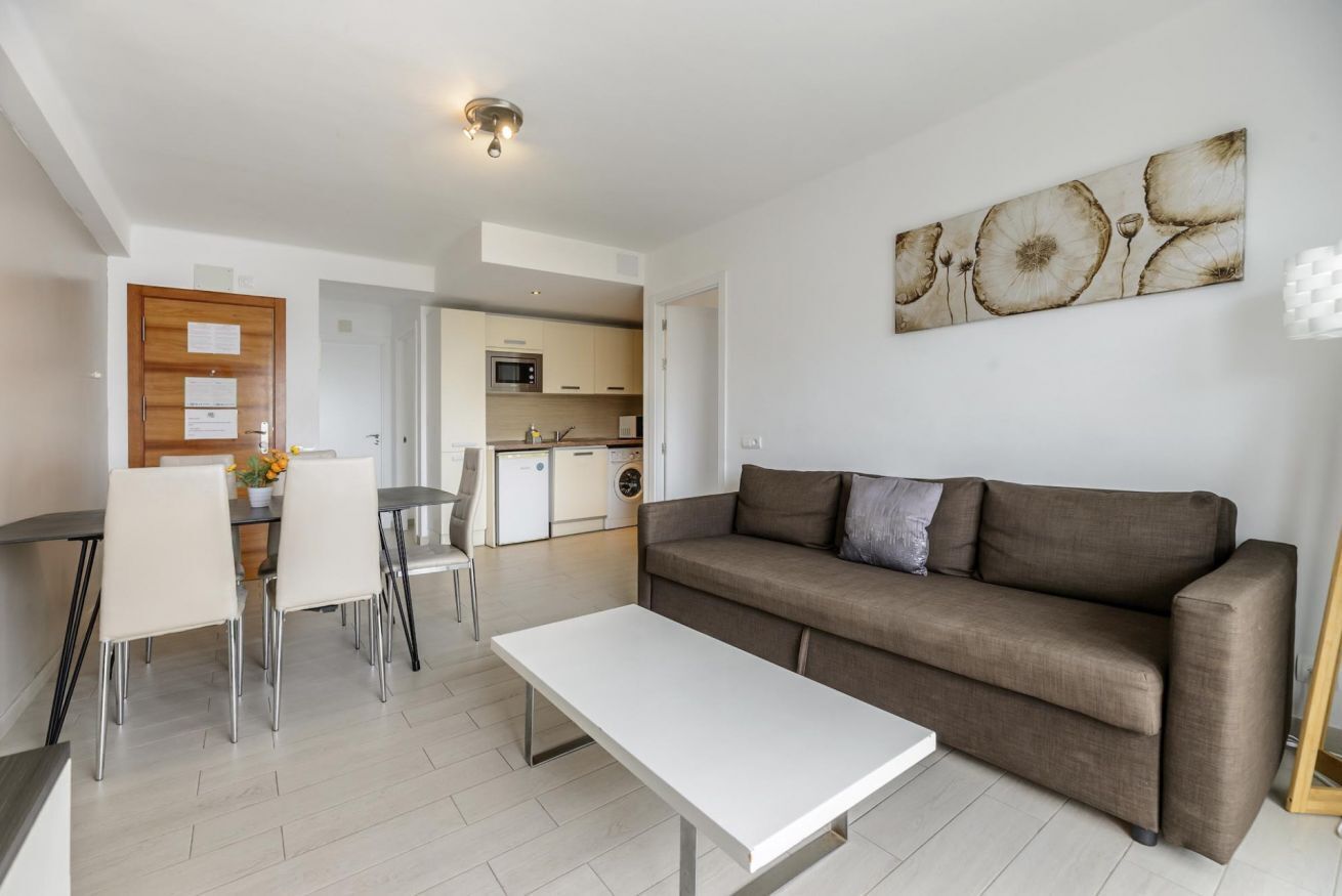 Een moderne woonkamer met een bank, eettafel, stoelen en een keuken op de achtergrond.