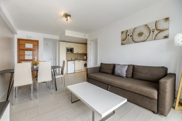 A modern living room with a sofa, dining table, chairs, and a kitchen in the background.