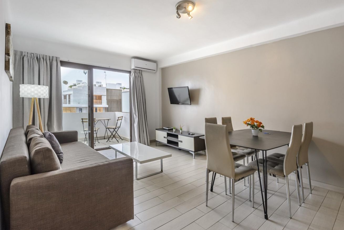 Een moderne woonkamer met een bank, eettafel, stoelen, een televisie en een balkon met gordijnen.