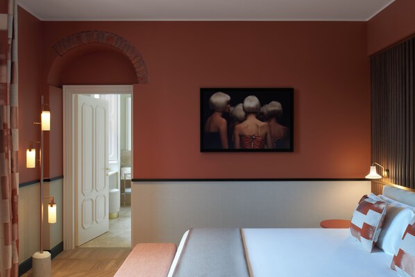 Una habitación de hotel con una cama, un cuadro en la pared, una puerta que da a un baño y un espejo.
