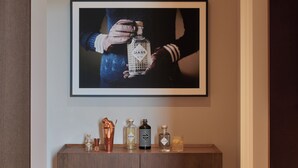 A framed artwork of hands holding a bottle, a wooden console table with various bottles, and a wooden floor. - Amabilia Suites (Milan)