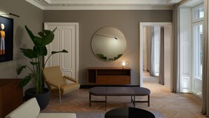 A spacious living room with a large potted plant, a round mirror, a wooden bench, and a beige armchair. - Amabilia Suites (Milan)