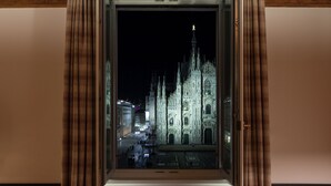 A view through a window with curtains, featuring a Gothic-style building with a spire, illuminated at night. - Amabilia Suites (Milan)