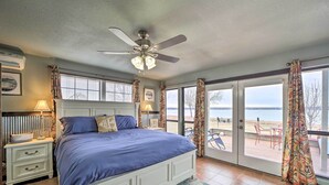 Una camera da letto con un letto grande, un ventilatore a soffitto e vista sulla spiaggia attraverso le porte scorrevoli in vetro.
