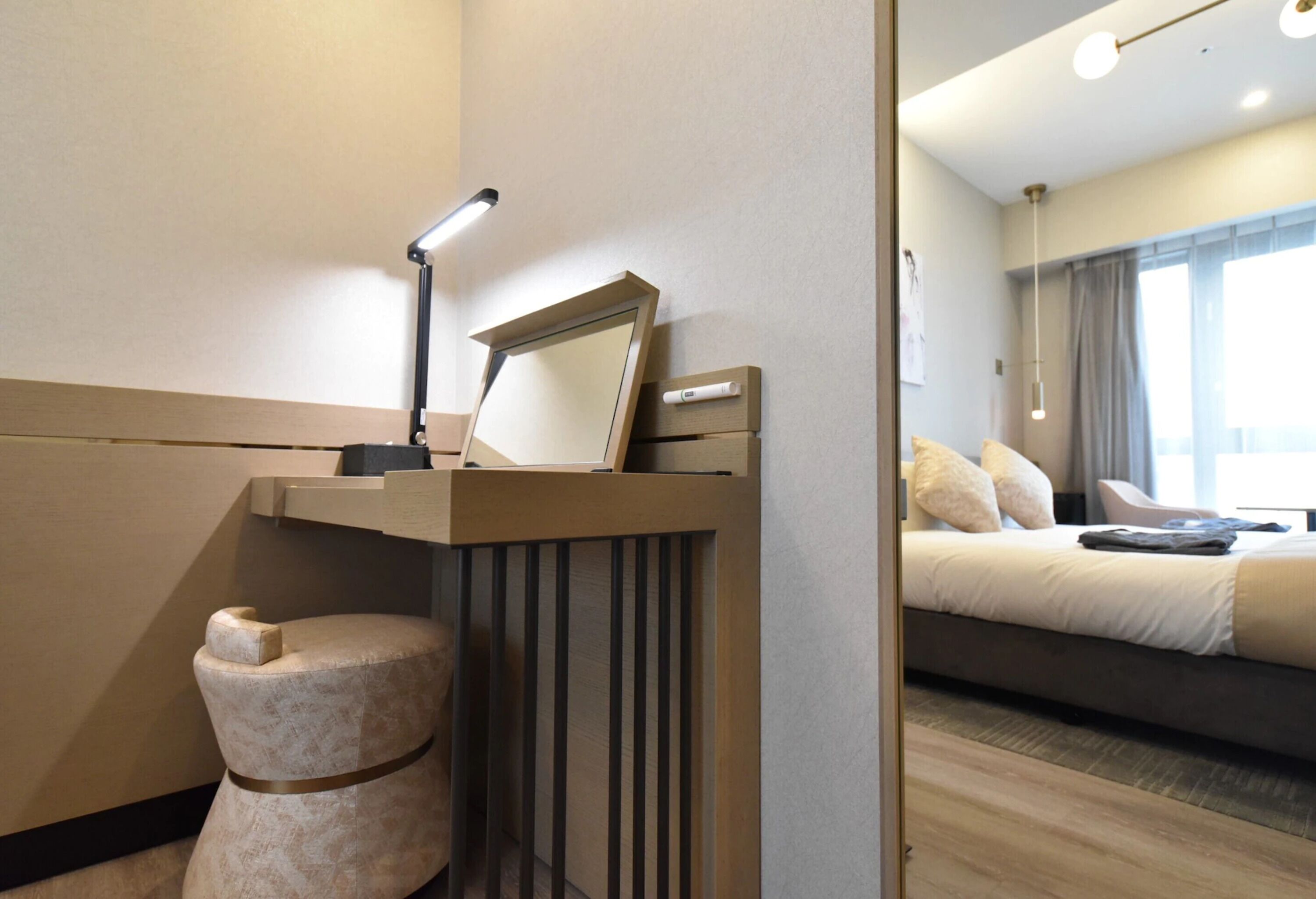 A modern hotel room with a wooden vanity, a mirror, a bedside table, and a bed with a view of the city.