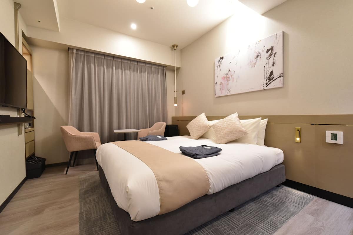 Een hotelkamer met een groot bed, een bureau, een stoel, een televisie en een schilderij aan de muur.