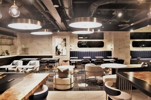 Un restaurante moderno con mesas redondas, asientos acolchados e iluminación colgante.