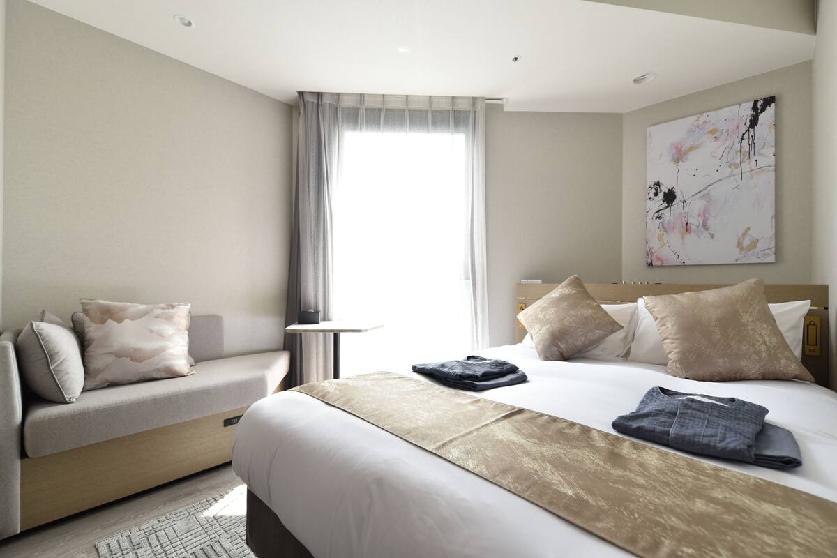 Een moderne hotelkamer met een bed, een bank, een klein tafeltje en een schilderij aan de muur.