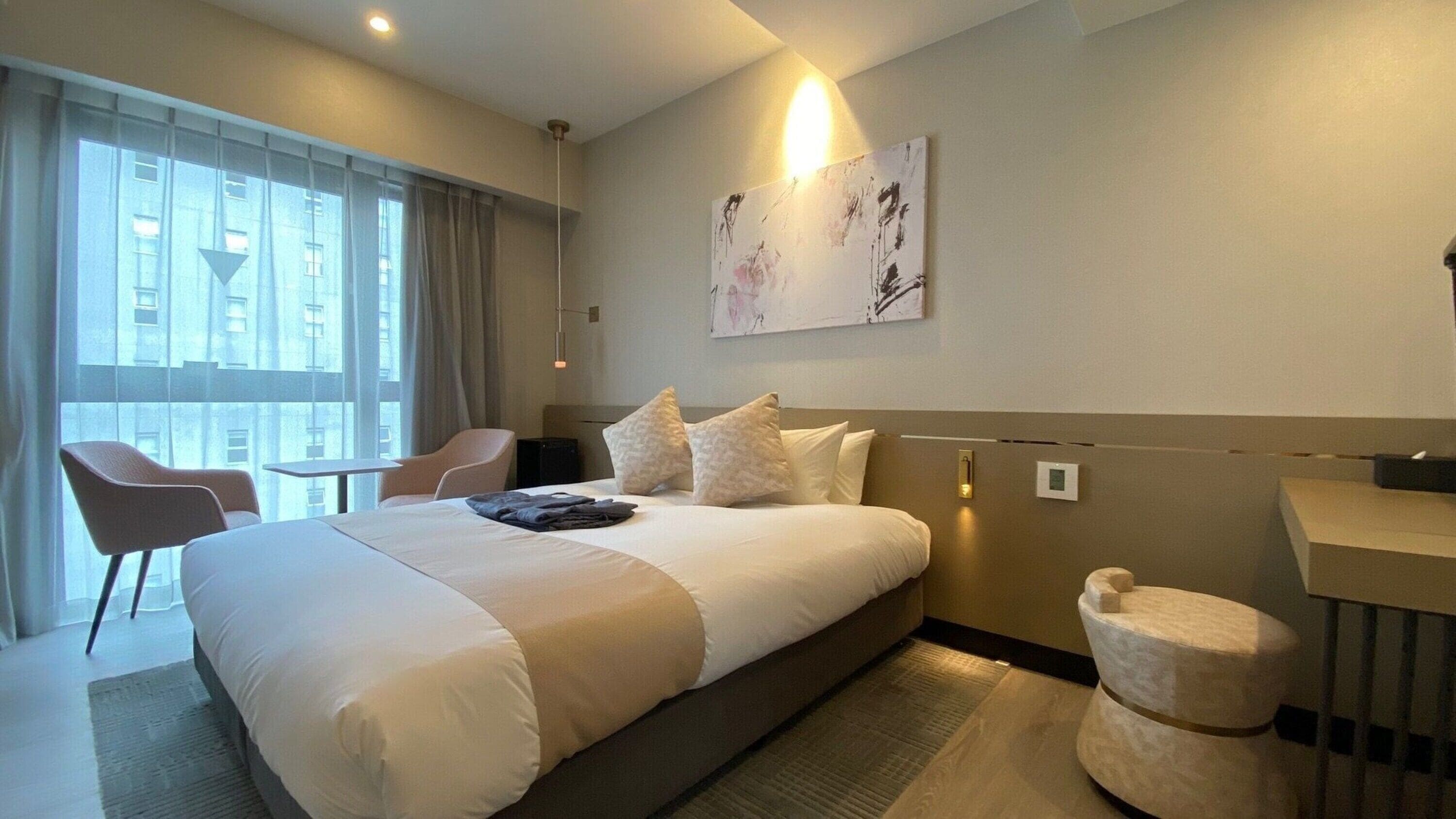 Habitación de hotel con una cama grande, un escritorio, una silla y un ventanal con cortinas.