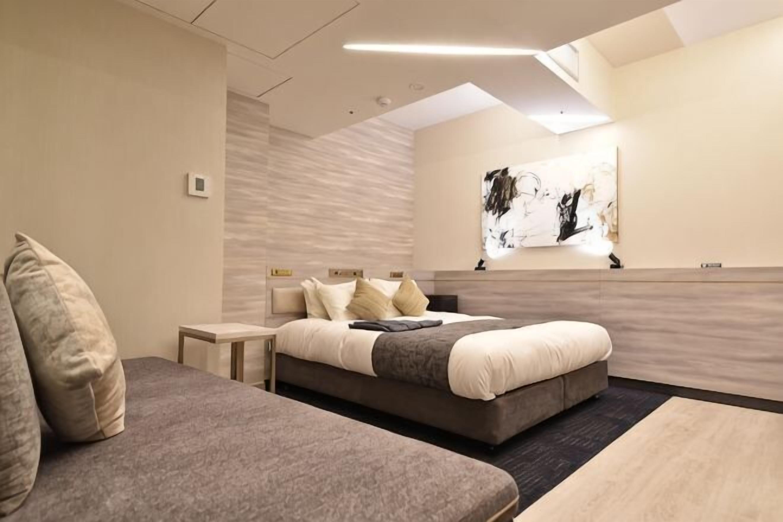 Ein modernes Hotelzimmer mit einem Bett, einer Couch, einem Nachttisch und einem Wandbild.