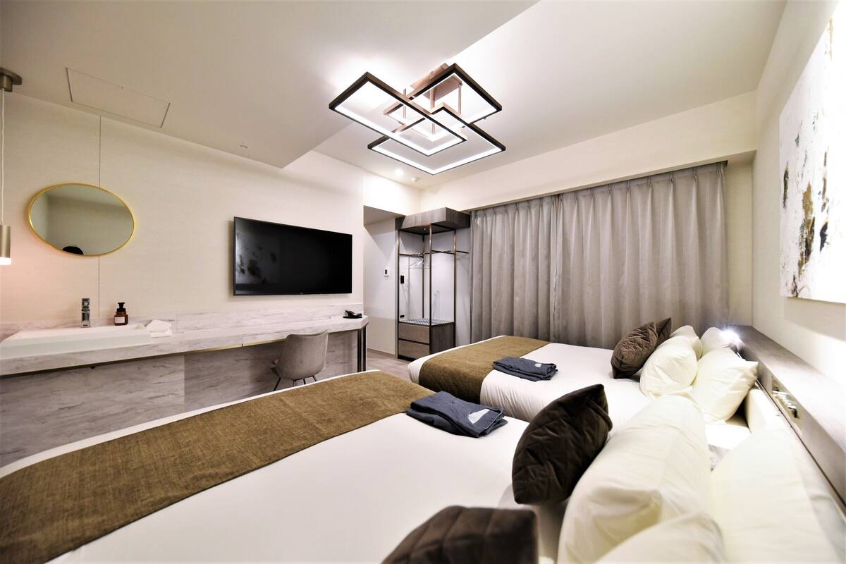 Een moderne hotelkamer met twee bedden, een grote spiegel, een flatscreen televisie, en een badkamer met douche en toilet.
