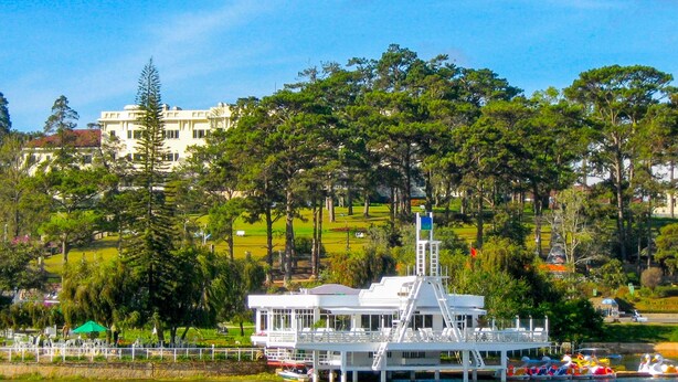 A white building with a balcony and a flag, surrounded by trees and a body of water. - Jolie House II - Villa 2 Double Rooms - Charming (Thành phố Đà Lạt)