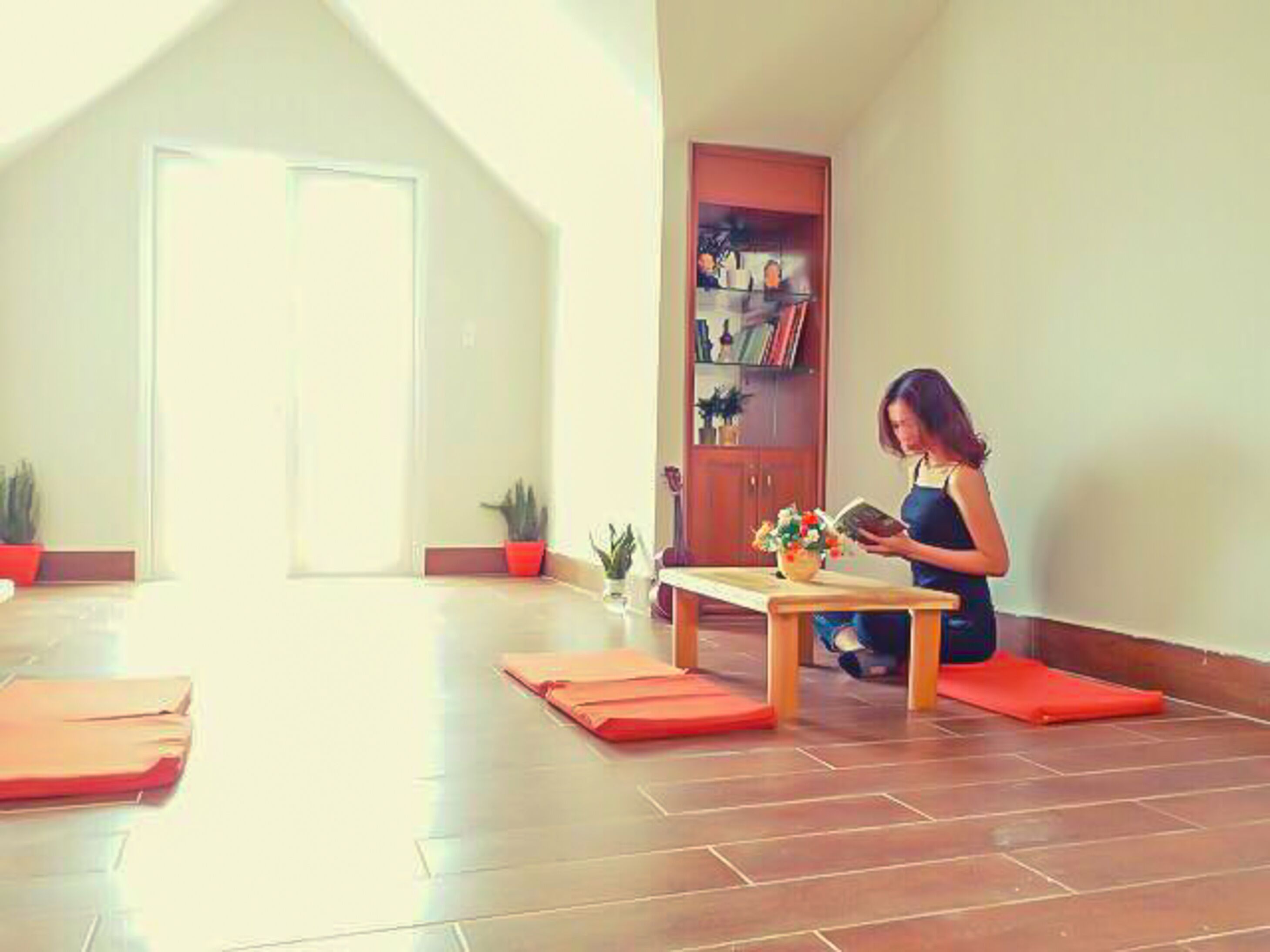 Ein Zimmer mit Holzboden, einem kleinen Tisch mit Blumenvase und einem Bücherregal.