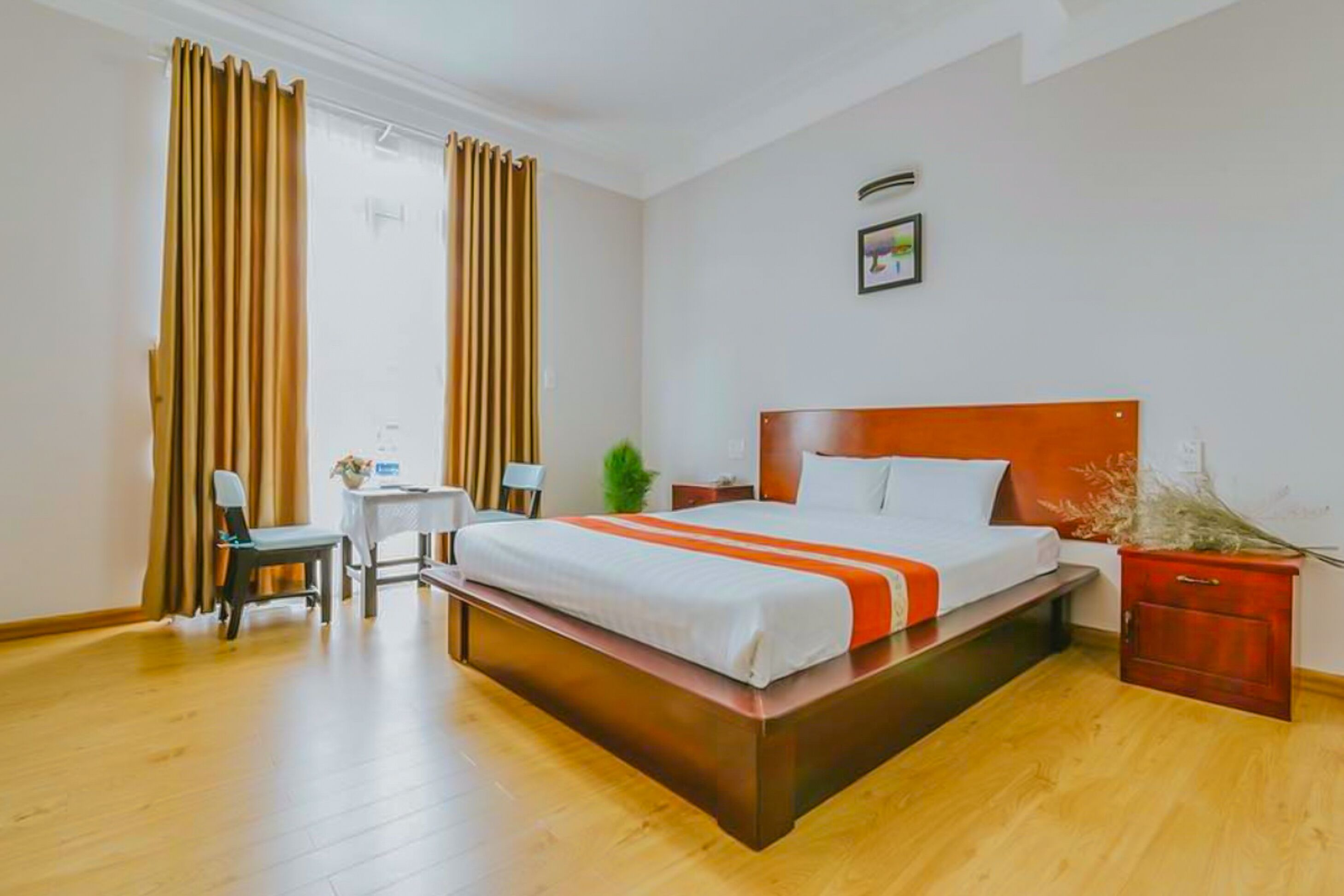 A hotel room with a large bed, a desk with a chair, a small table, and a nightstand.