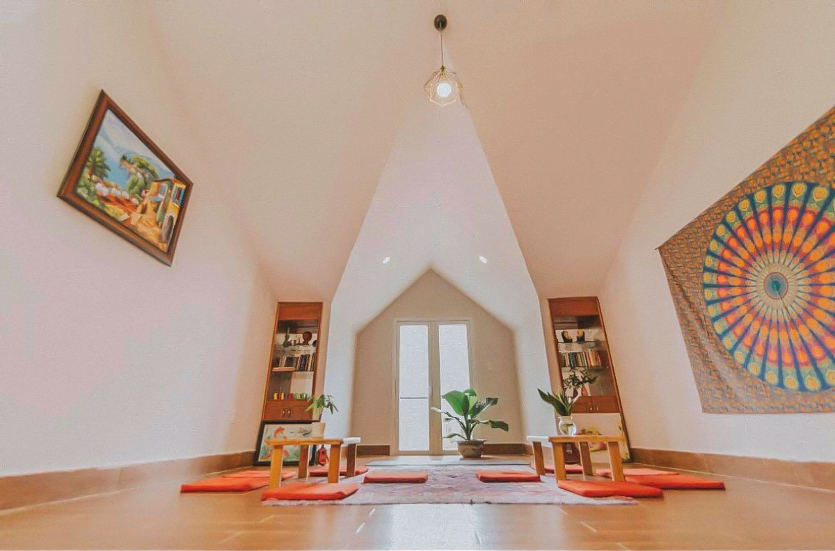 A spacious room with a high ceiling, a large window, and a colorful tapestry on the wall.