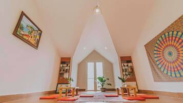 A spacious room with a high ceiling, a large window, and a colorful tapestry on the wall.
