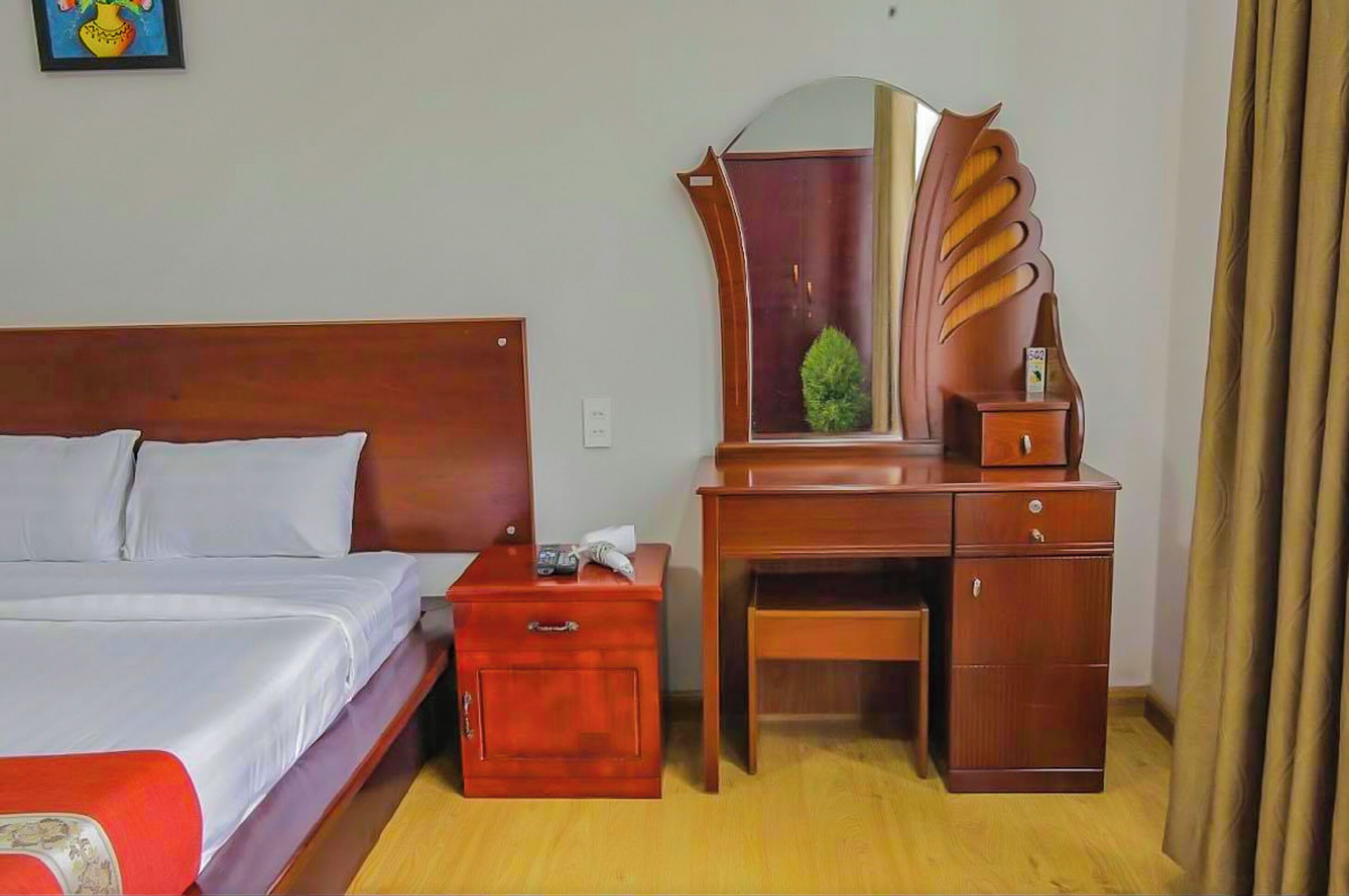 A hotel room with a wooden bed, a nightstand with a lamp, a dresser with a mirror, and a small table.