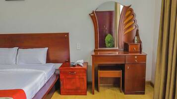 A hotel room with a wooden bed, a nightstand with a lamp, a dresser with a mirror, and a small table.