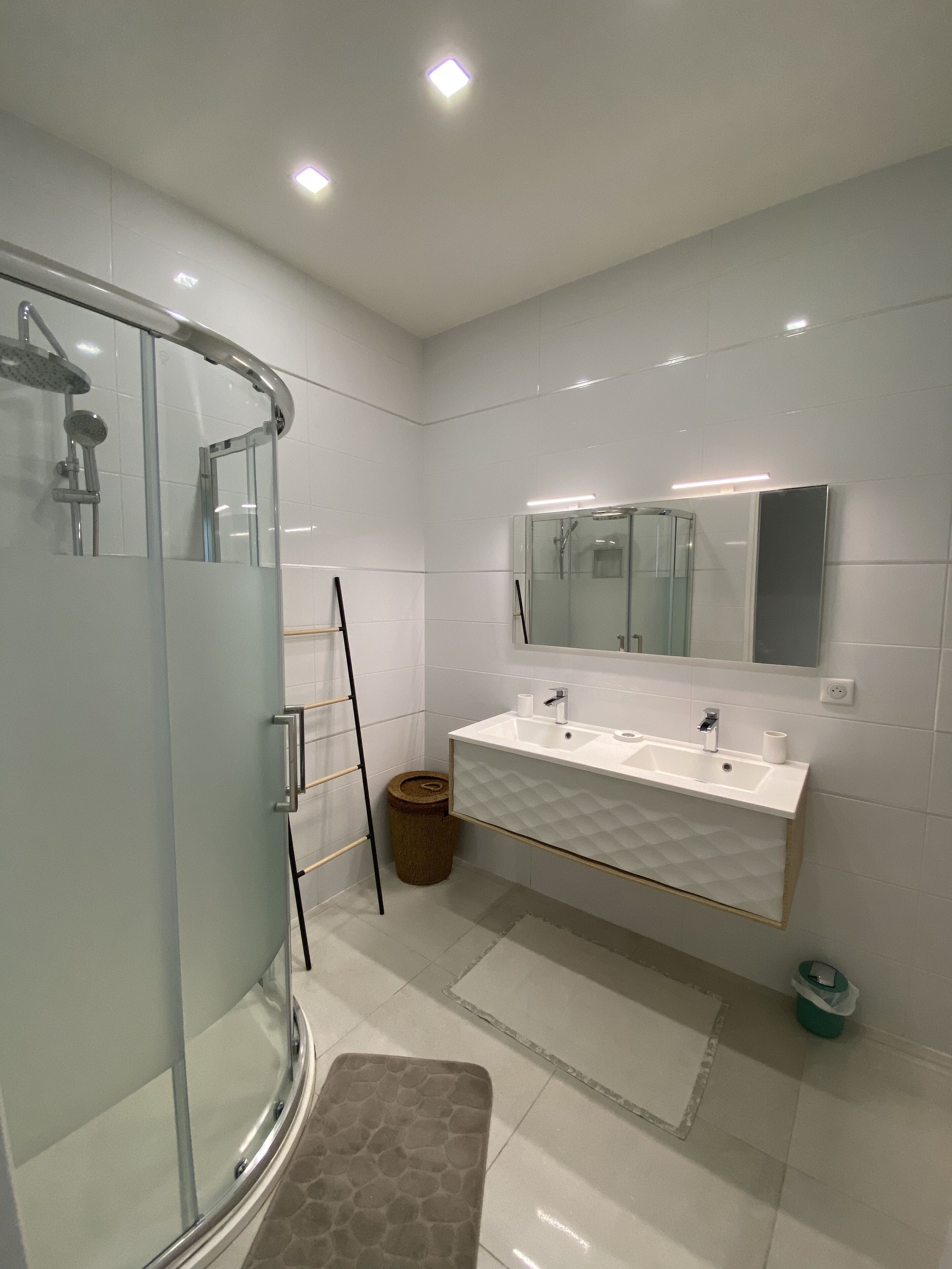Un bagno moderno con cabina doccia in vetro, un mobile lavabo bianco con un ampio specchio e pavimento piastrellato.