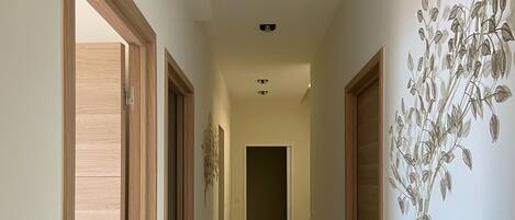 A hallway with wooden doors on either side, a light-colored tiled floor, and a wall-mounted decorative plant.