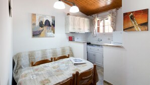 Un comedor con una mesa lista para dos personas, sillas de madera y un ventanal con cortinas.