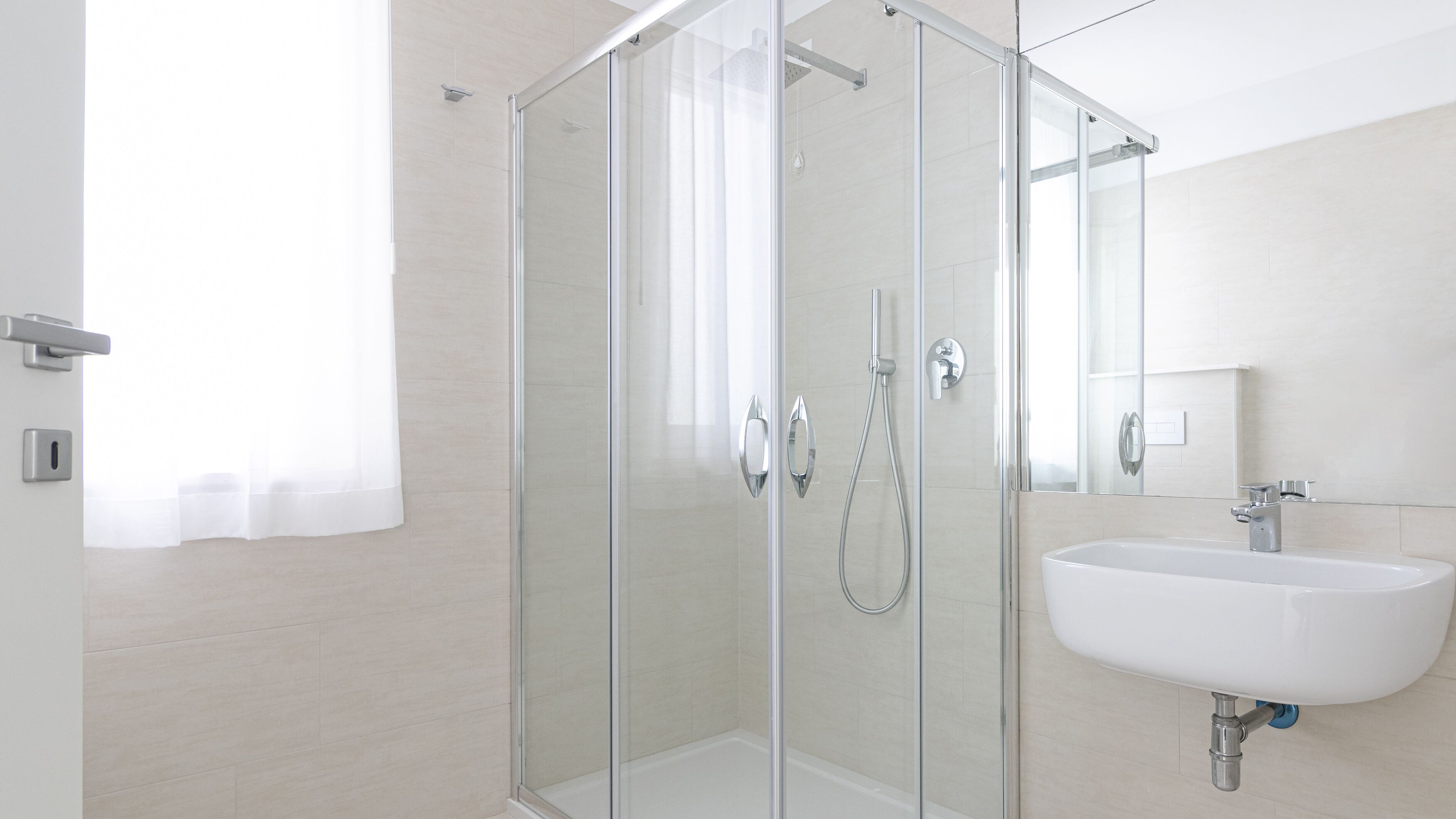 Een moderne badkamer met een douchecabine van glas, een witte wastafel en een spiegel.