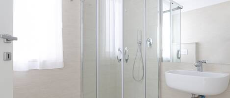 Een moderne badkamer met een douchecabine van glas, een witte wastafel en een spiegel.