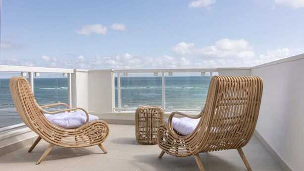 Un balcon avec deux fauteuils en osier et un petit pouf, donnant sur l’océan.